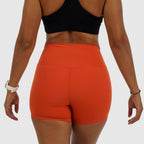 Back view of bright orange athletic shorts with reflective logo