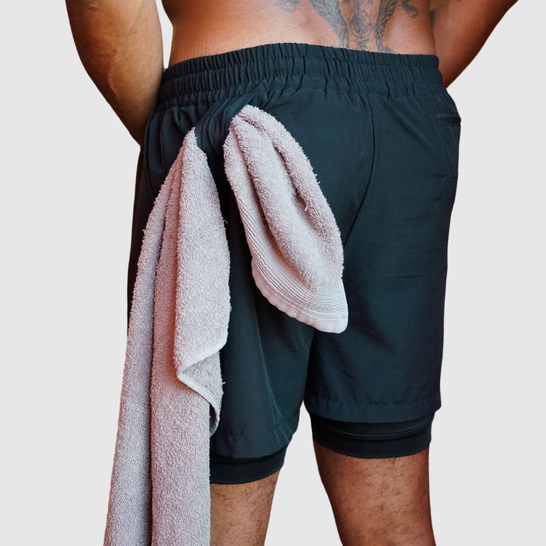 Model using the towel loop on the black Elite shorts to hold a white gym towel.